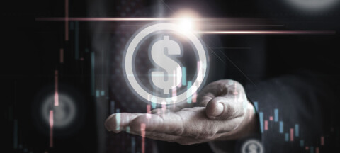 Businessperson’s hand holding a glowing digital dollar symbol with stock charts overlay