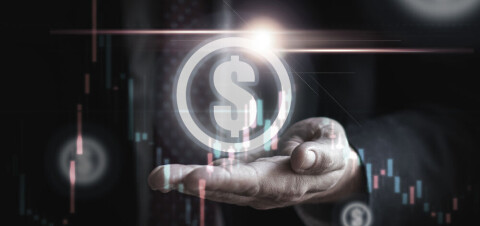 Businessperson’s hand holding a glowing digital dollar symbol with stock charts overlay